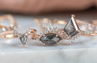 Three rings on a marble counter top spread in a horizontal line. Two of which are a triangle shape and one an oval. They have smaller diamonds outlining the big diamond in the center. 