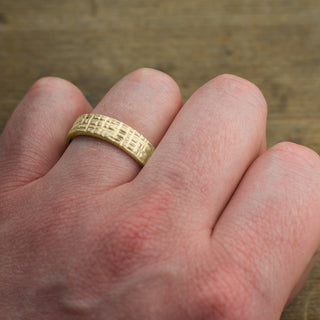 Perfect men's accessory, a 6mm 14k yellow gold wedding band with a distinct textured matte finish, displayed from top view