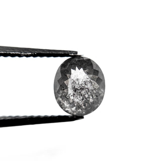 Close-up of a 1.94 Carat Salt and Pepper Double Cut Oval Diamond held by black tweezers, showcasing its unique speckled inclusions and eco-friendly craftsmanship.