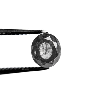 Close-up view of a 1.94 Carat Salt and Pepper Double Cut Oval Diamond held by black tweezers, showcasing its unique speckled inclusions and faceted surface.