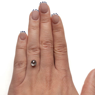 Close-up of a hand displaying a 1.94 Carat Salt and Pepper Double Cut Oval Diamond, emphasizing its unique speckled texture, handcrafted with eco-friendly and conflict-free materials.
