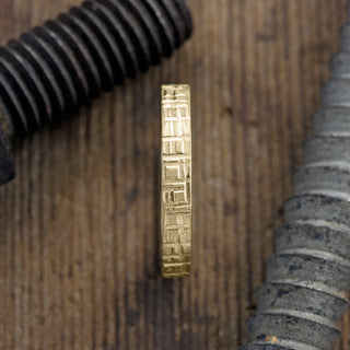 Angled perspective of a 4mm 14k yellow gold men's wedding band with unique geometric texture