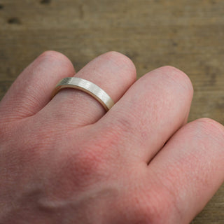 The elegant simplicity of the 4mm 14k White Gold Men's Wedding Band with matte finish, showcased on a stand